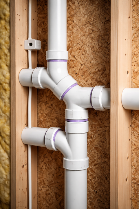 PVC plumbing pipes and fittings inside an unfinished wall frame with white and purple primer joints