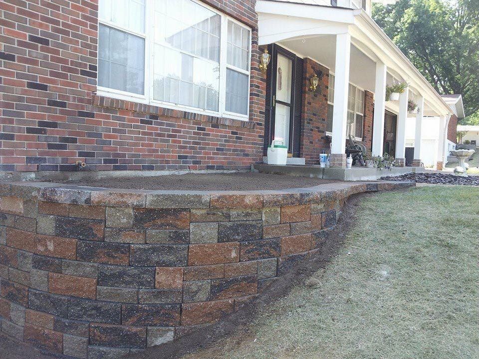 Brick retaining wall in front of a brick house with a porch.
