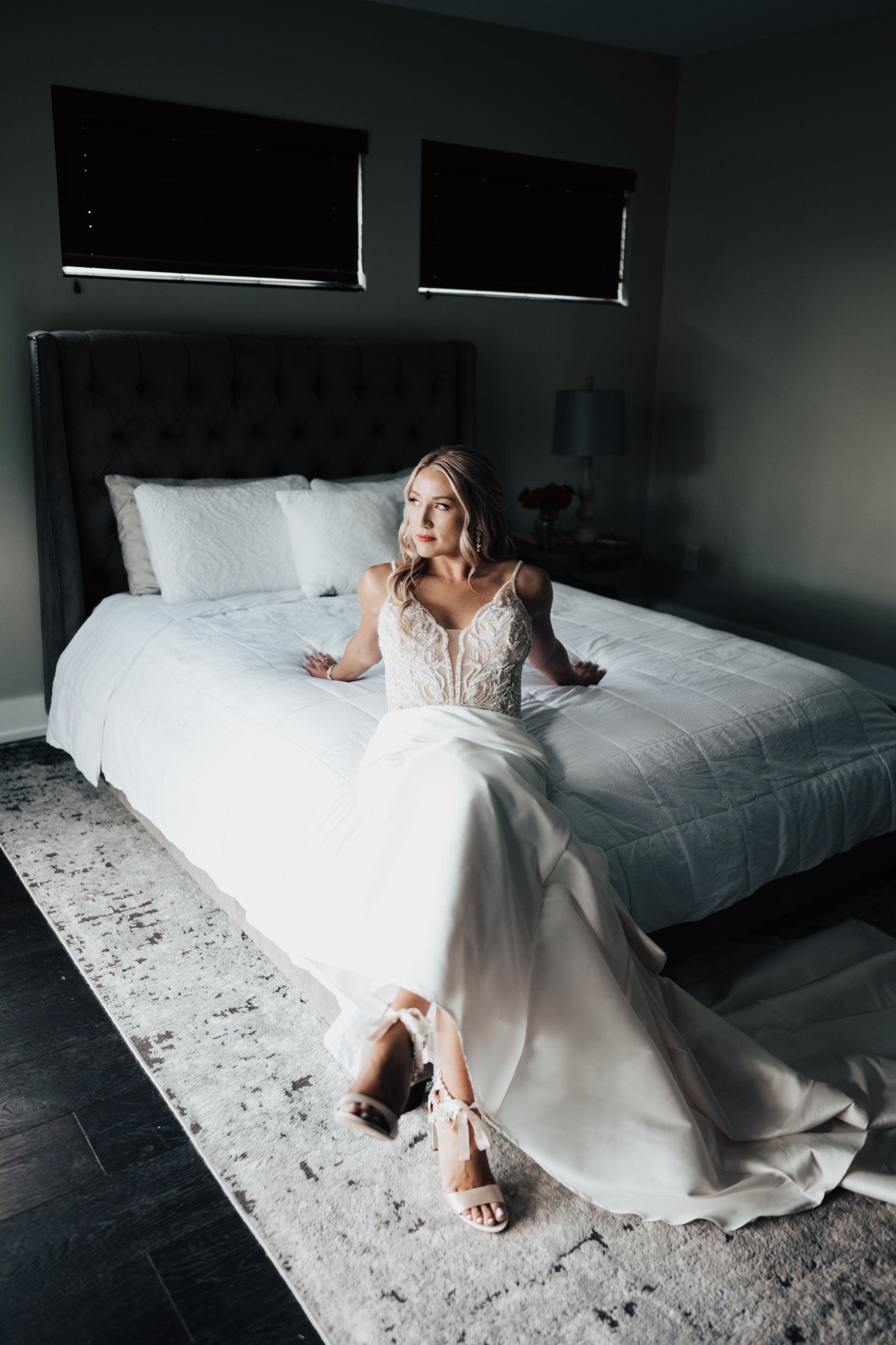 Woman in wedding dress sitting on bed, looking to the side. Light and airy scene.