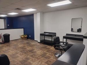 Empty office room with blue accent wall, desks, chairs, mirror, trash can, and tiled floor.