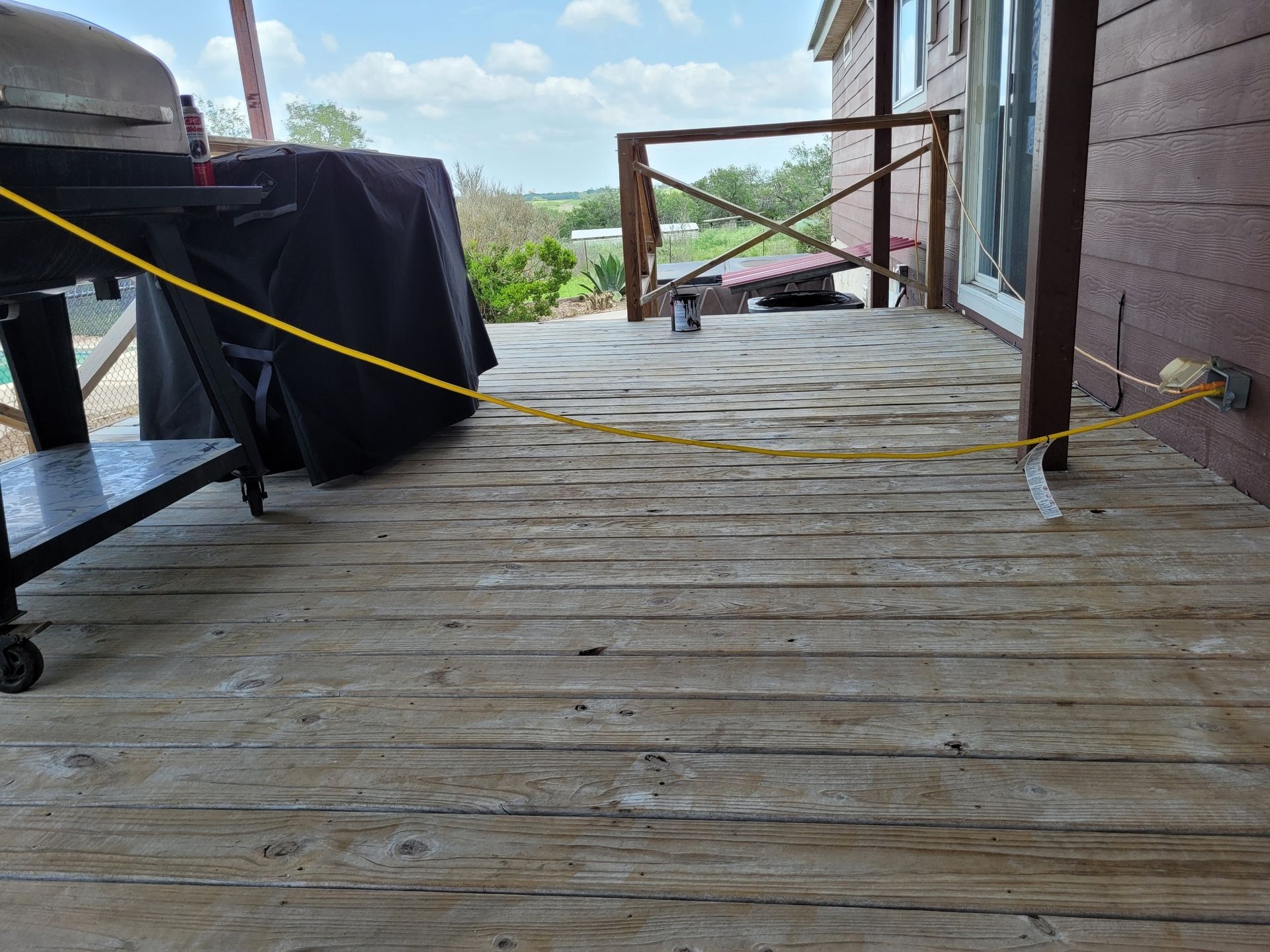 Wooden porch deck with yellow safety ropes and a covered table, overlooking a cloudy outdoor view