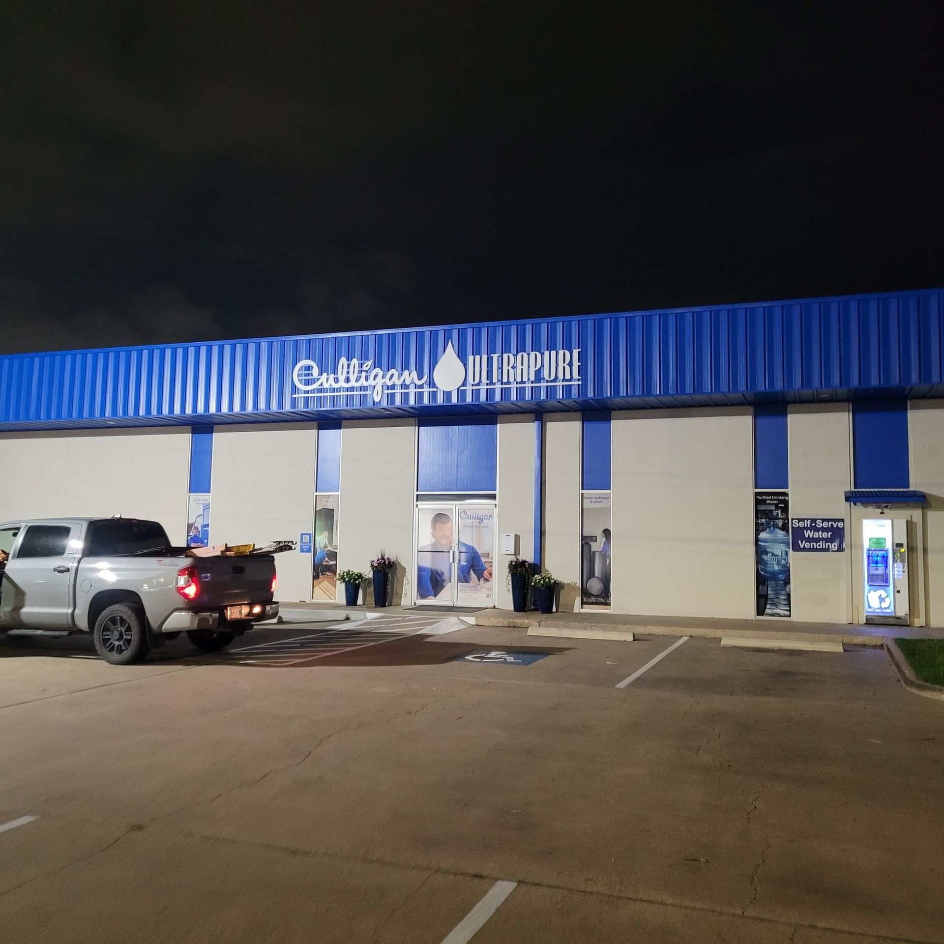 Nighttime view of a blue-lit commercial building with parked SUV in front