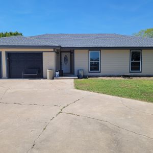 Single-story beige house with a dark gray garage door, driveway, and small front lawn under a blue sky