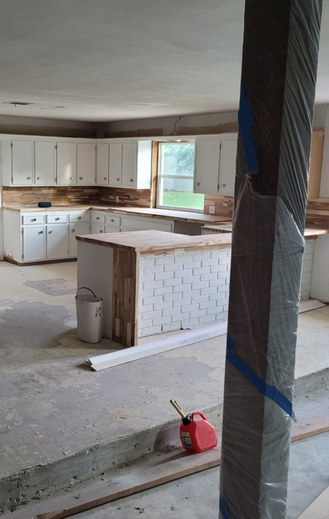 Unfinished kitchen with white cabinets, central island, exposed columns, and construction tools on the floor.