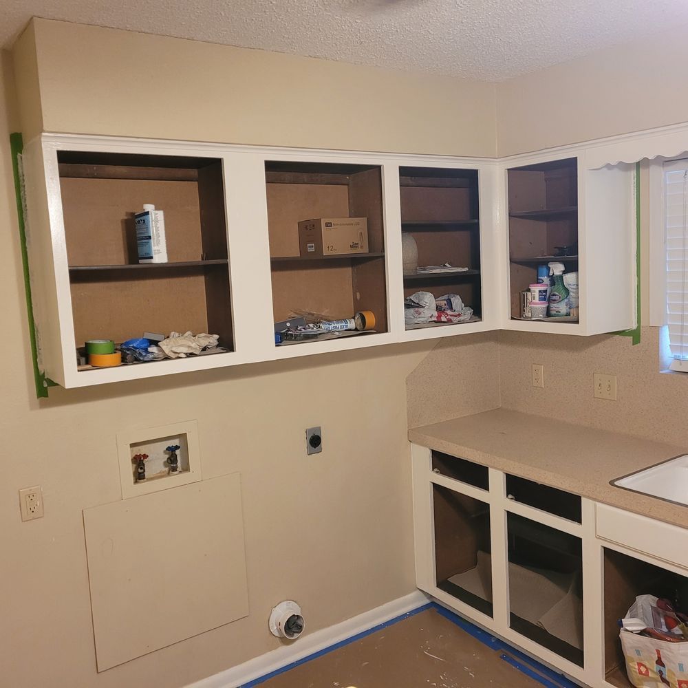 Kitchen with white cabinets and open shelves, beige walls, and unfinished lower cabinet area with masked floor.