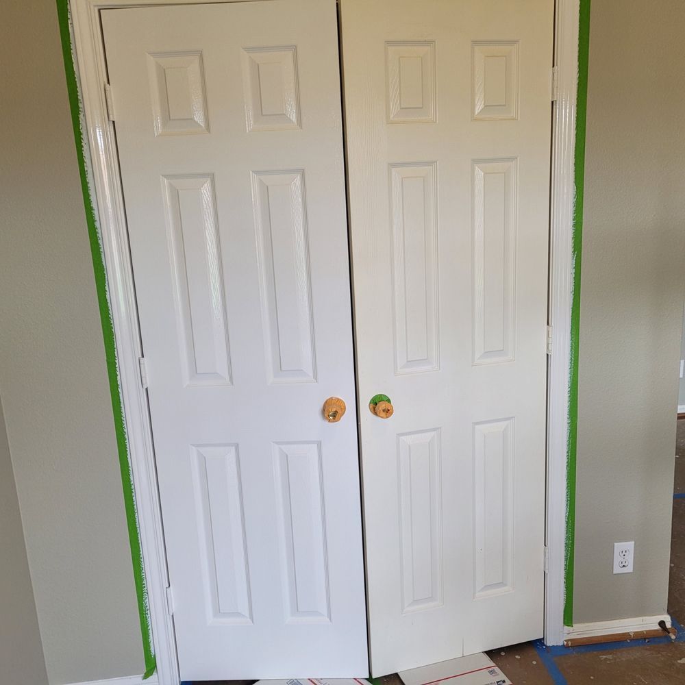 White double closet doors painted with green tape around the frame in a room with bare walls.