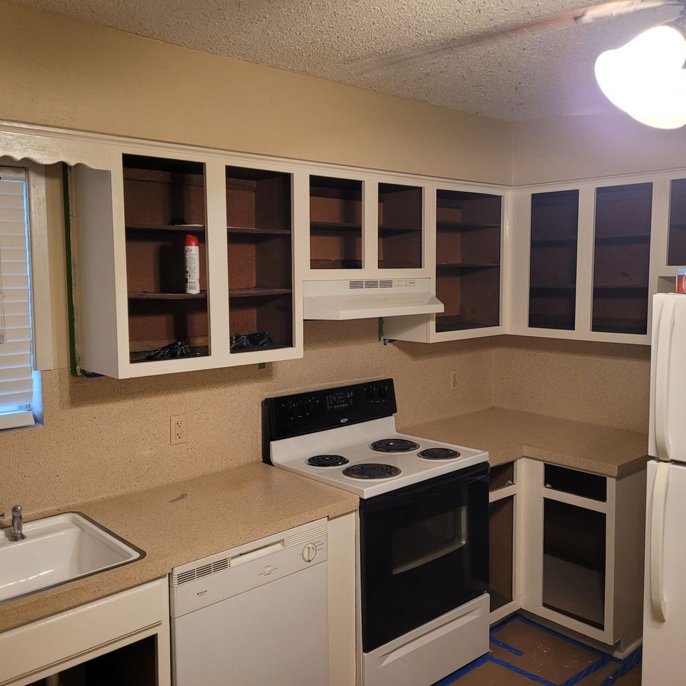 Small beige kitchen with white appliances and open cabinet doors above the stove and sink.