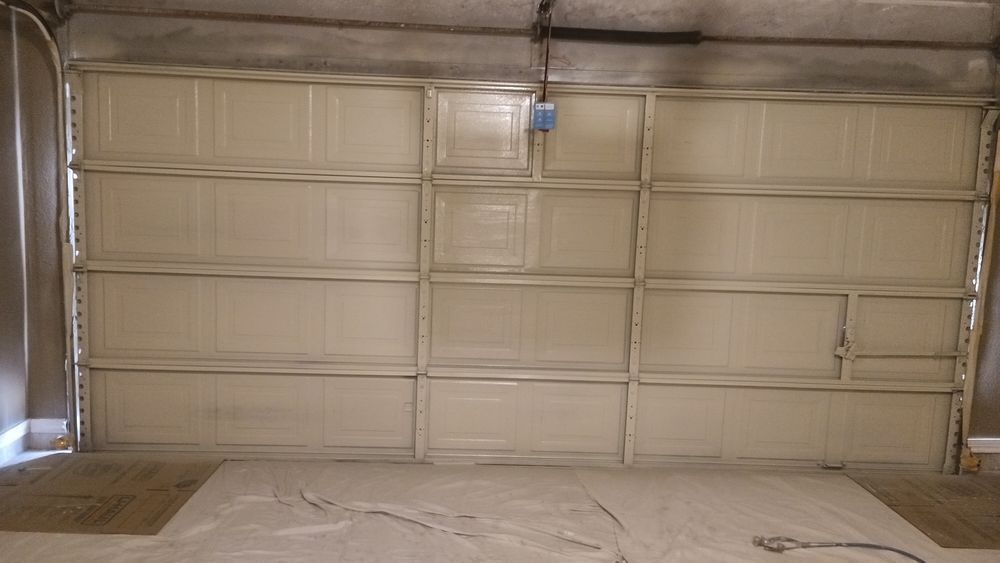 Empty garage interior with a closed beige roll-up door and covered floor