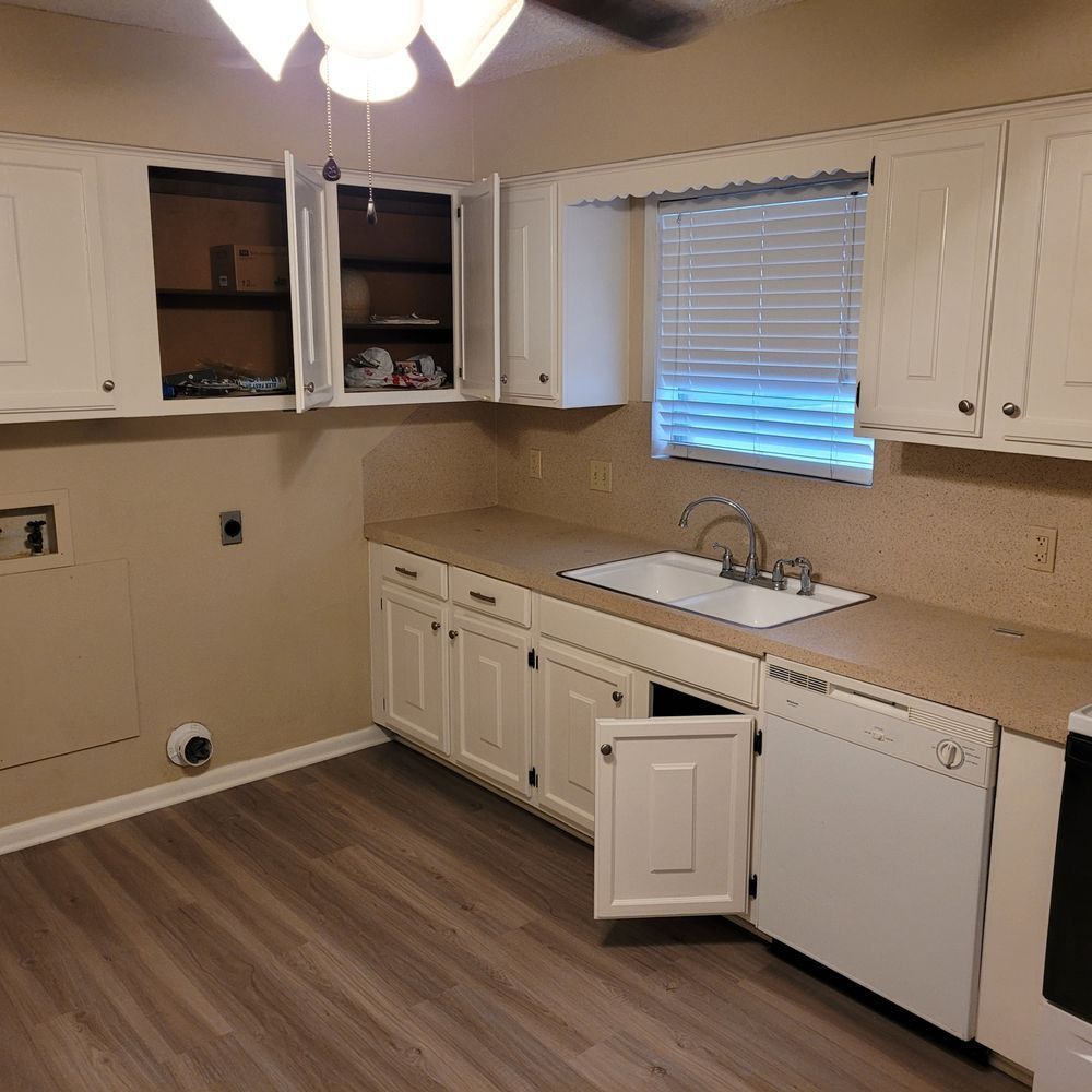 Empty kitchen with white cabinets, beige countertops, a sink, and wood-look flooring.