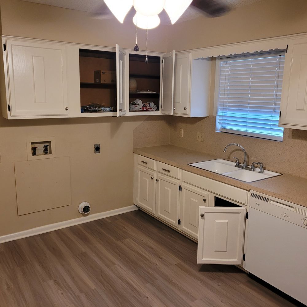 Empty kitchen with white cabinets, wood-look floor, sink under window, and a partially open dishwasher