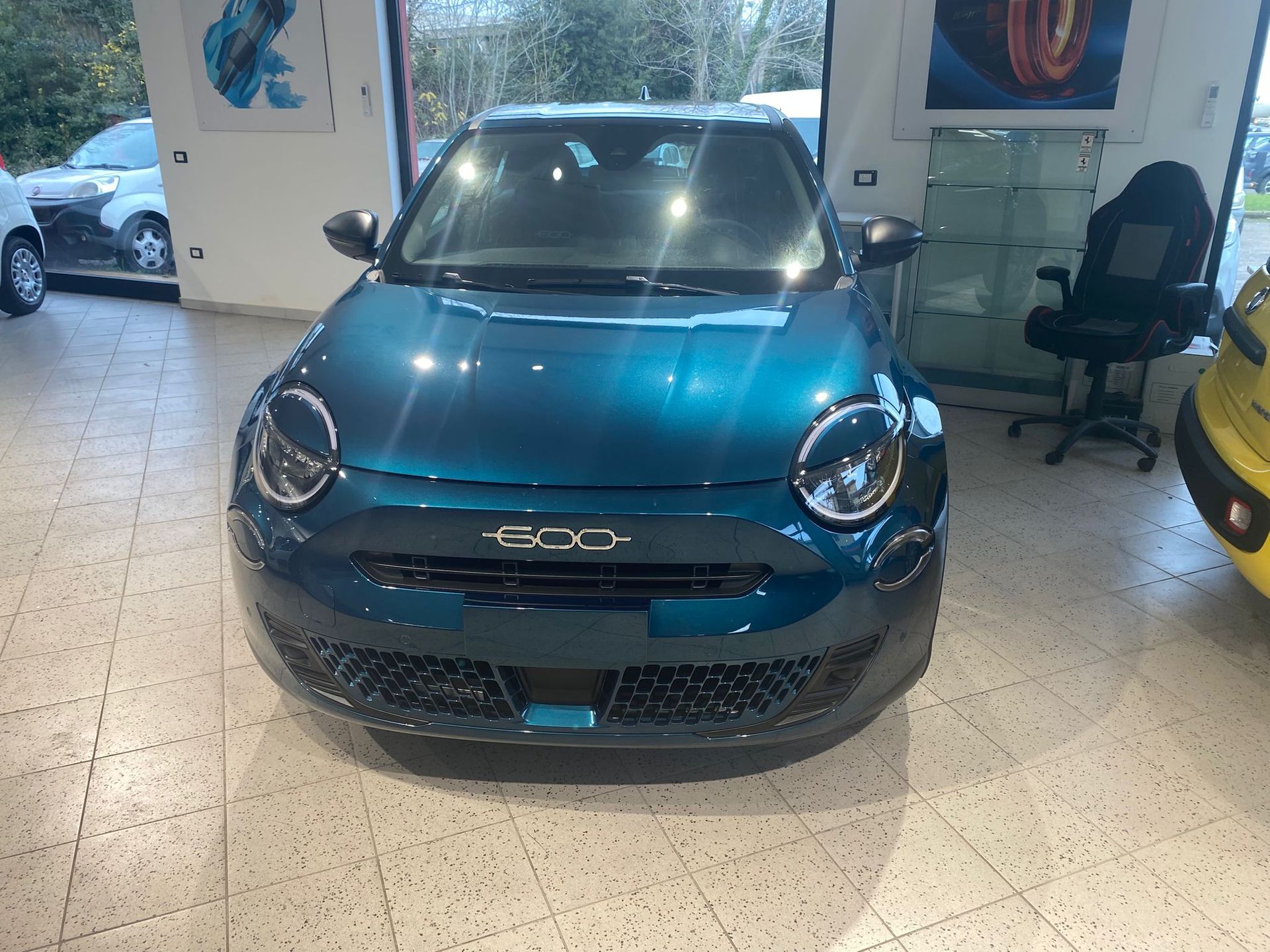 Auto compatta blu esposta all'interno di uno showroom, vista frontale con fari e griglia visibili.