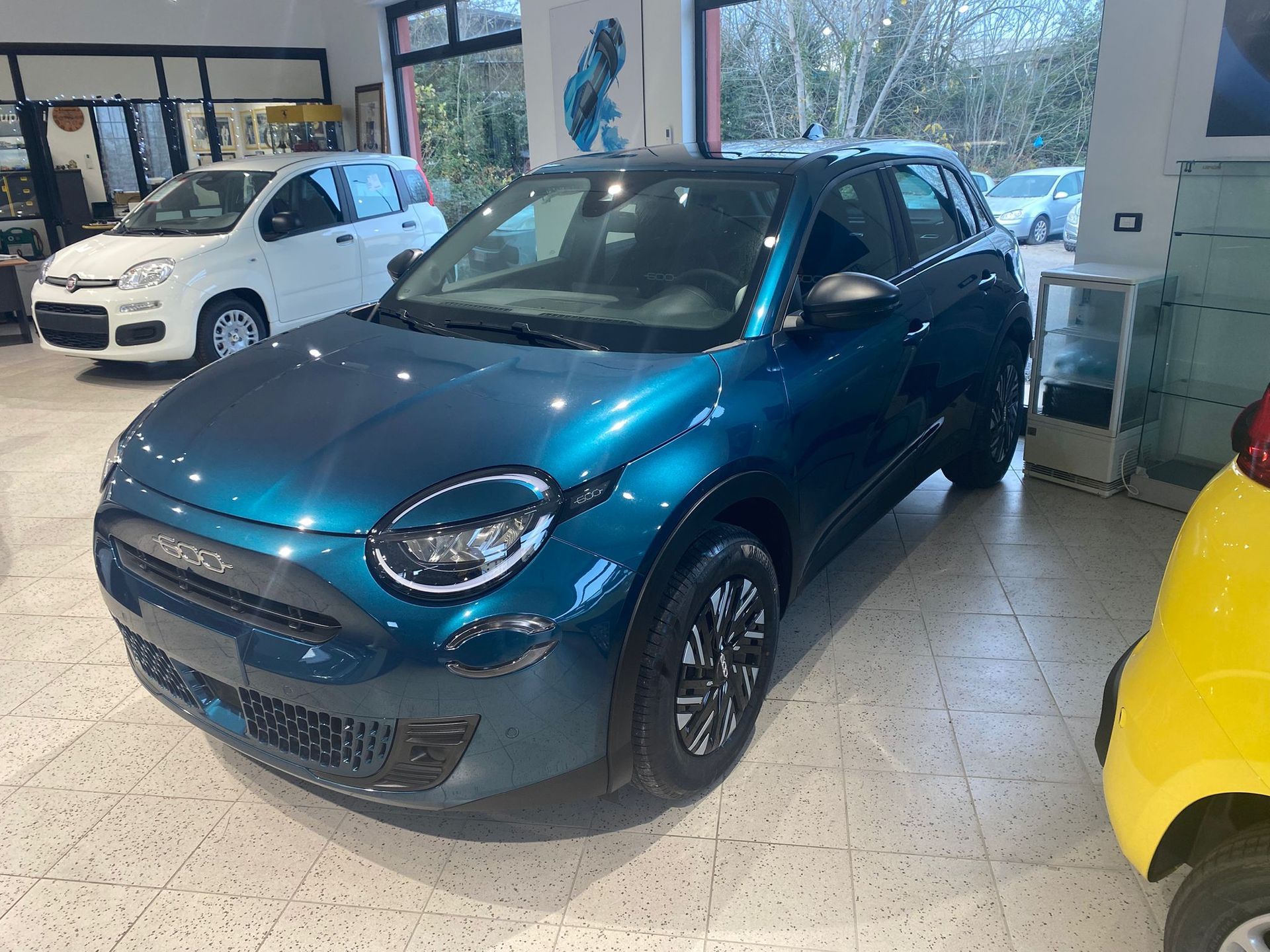 SUV compatto blu in uno showroom, con un'auto bianca sullo sfondo e un'auto gialla sul lato destro.