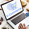 Laptop displaying “E-Commerce” on a desk with a hand using a mouse nearby