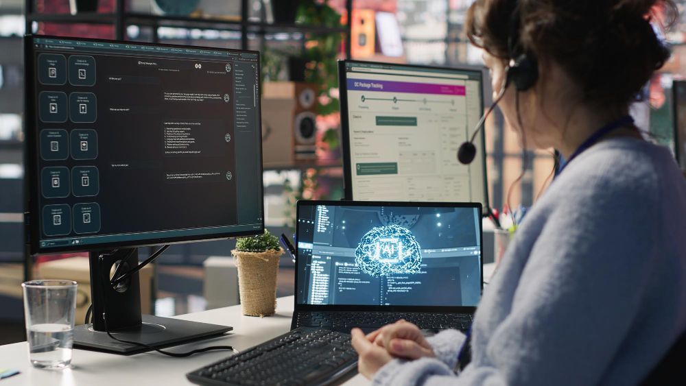 Person wearing a headset works at a desk with multiple monitors displaying code and a laptop.