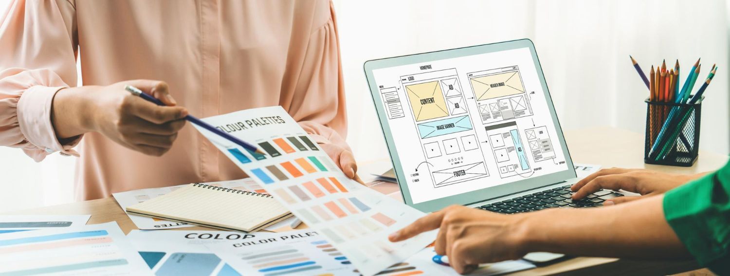 Two people reviewing color swatches and design mockups beside a laptop on a desk