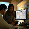 Two people reviewing data on a desktop monitor in a dimly lit office