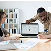 Team meeting around a laptop in a bright office, discussing a chart on the screen