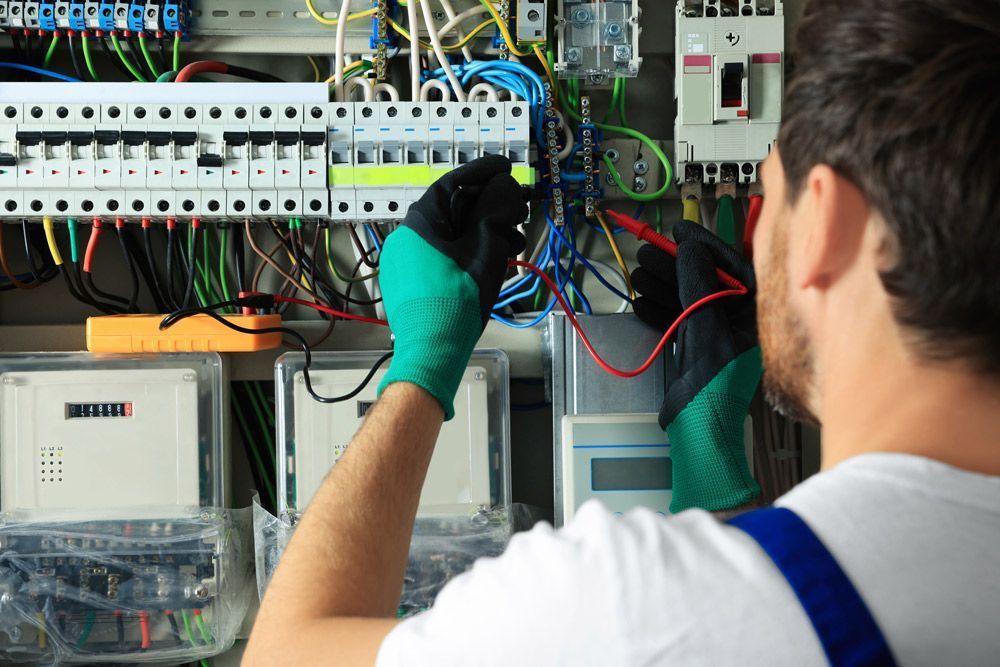 Electrician working on a switchboard with multiple circuit breakers and wiring.
