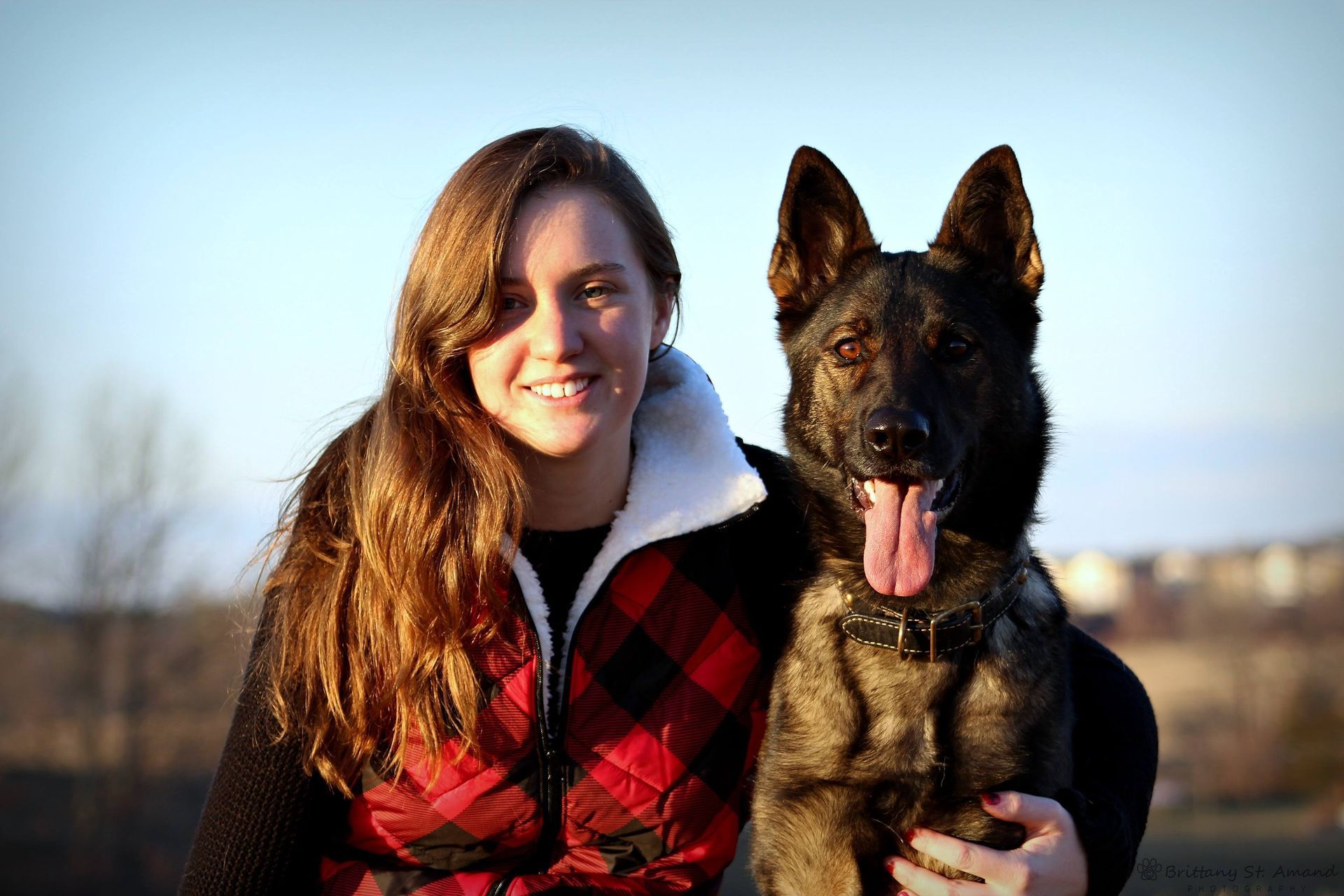 Woman in a red plaid jacket with a German shepherd outdoors, both facing the camera.