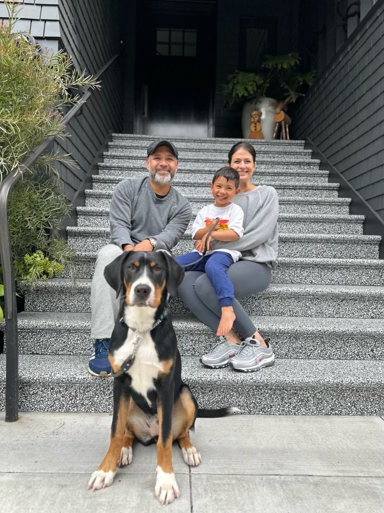 Family sitting on front steps with a large dog in the foreground, a cat on the stairs behind.