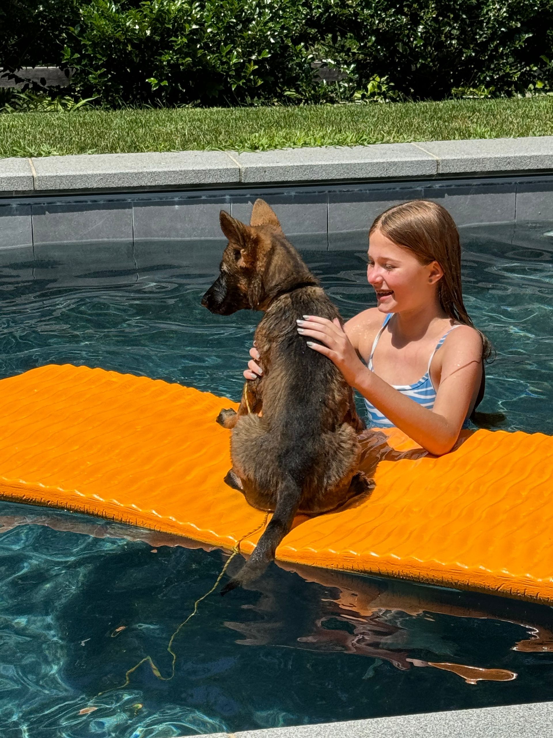 Girl holding a German shepherd on an orange float in a pool