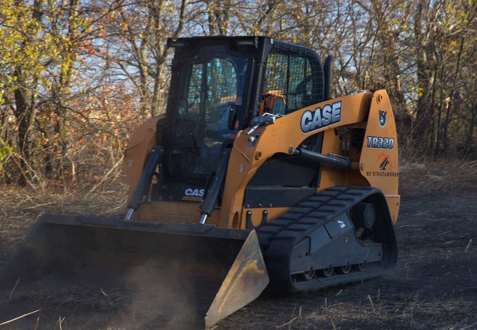 A white Bobcat track loader with a full bucket of dirt on a worksite in bright sunlight.