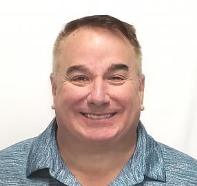 Smiling man in a blue collared shirt against a white background