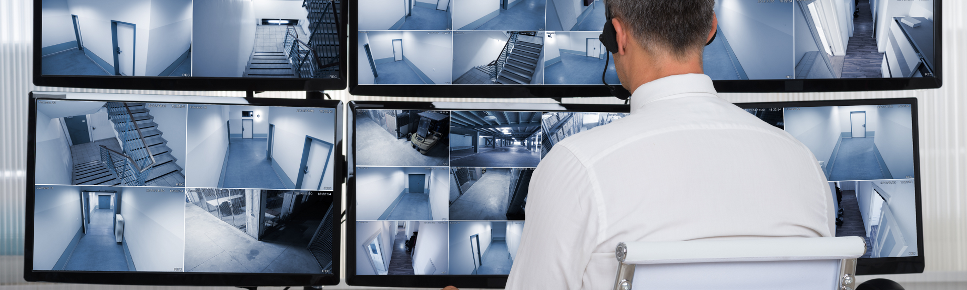Person monitoring multiple security camera feeds on wall-mounted screens in a control room