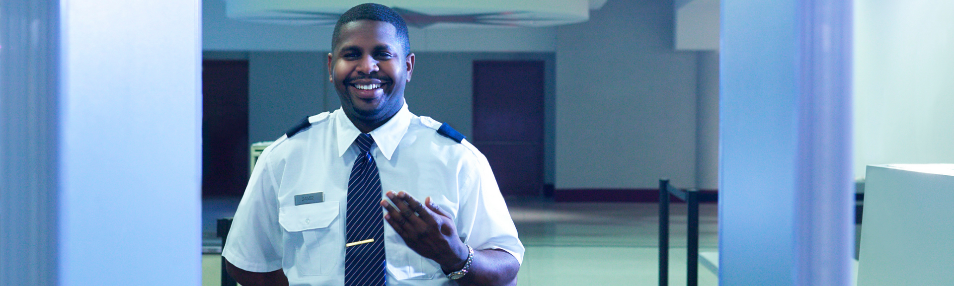 Smiling security guard in white shirt and tie standing in a hallway between blue doors
