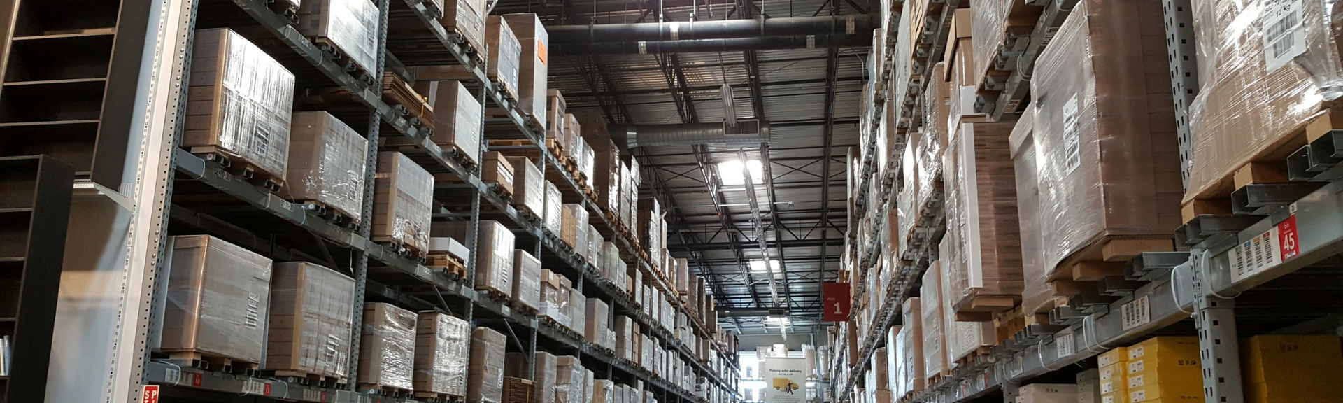 Warehouse aisle with tall shelves stacked with boxed inventory under bright overhead lights