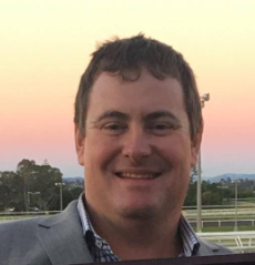 A man in a suit is smiling in front of a sunset.