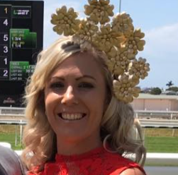 A woman wearing a red dress and a hat with flowers on it is smiling.