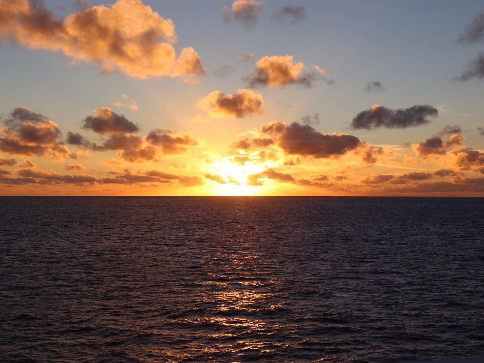 The sun is setting over the ocean with clouds in the sky