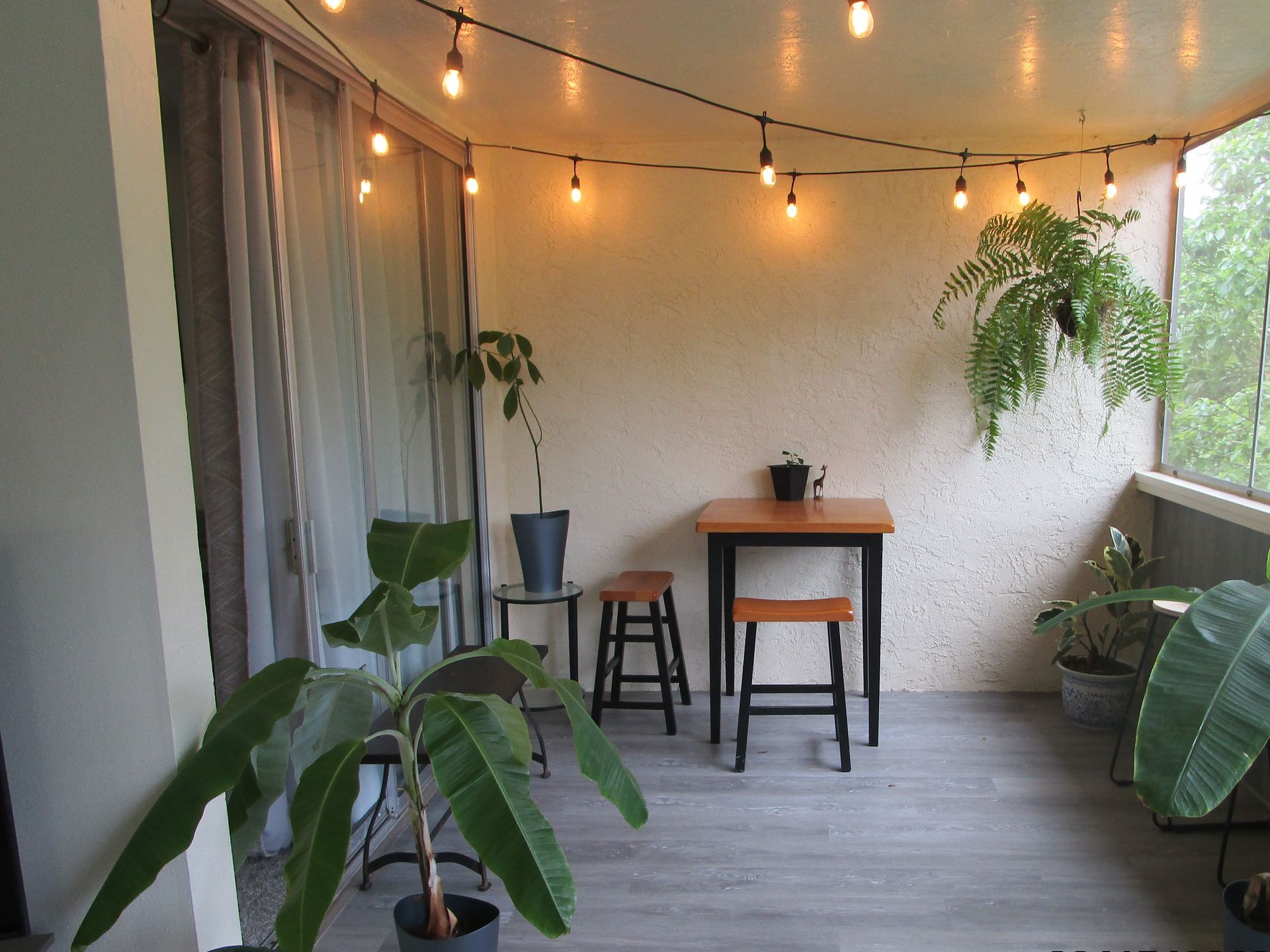 A balcony with a table and stools and a string of lights