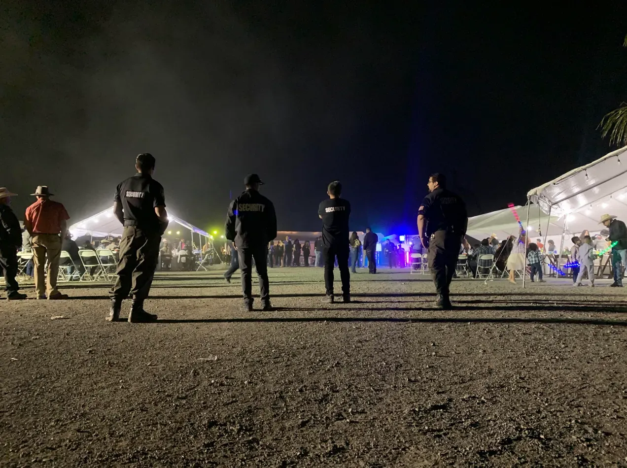 A group of people are standing in a parking lot at night.