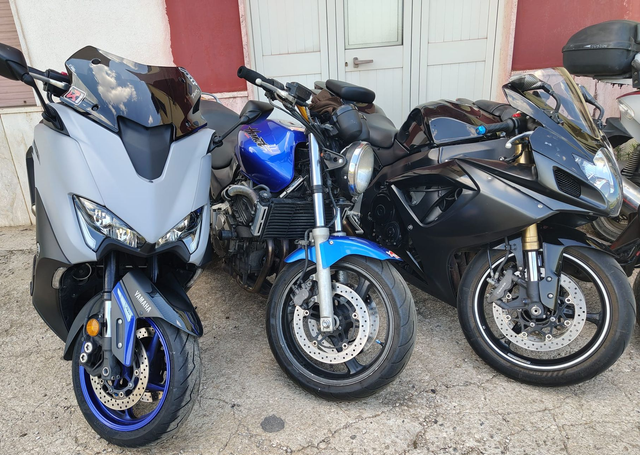 Tre scooter parcheggiati uno accanto all'altro all'esterno, per lo più grigi e blu con dettagli neri.