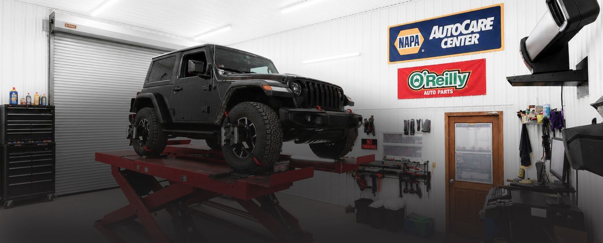 Black Jeep SUV in a cluttered garage under exposed beams and fluorescent lights | Pine Island Auto
