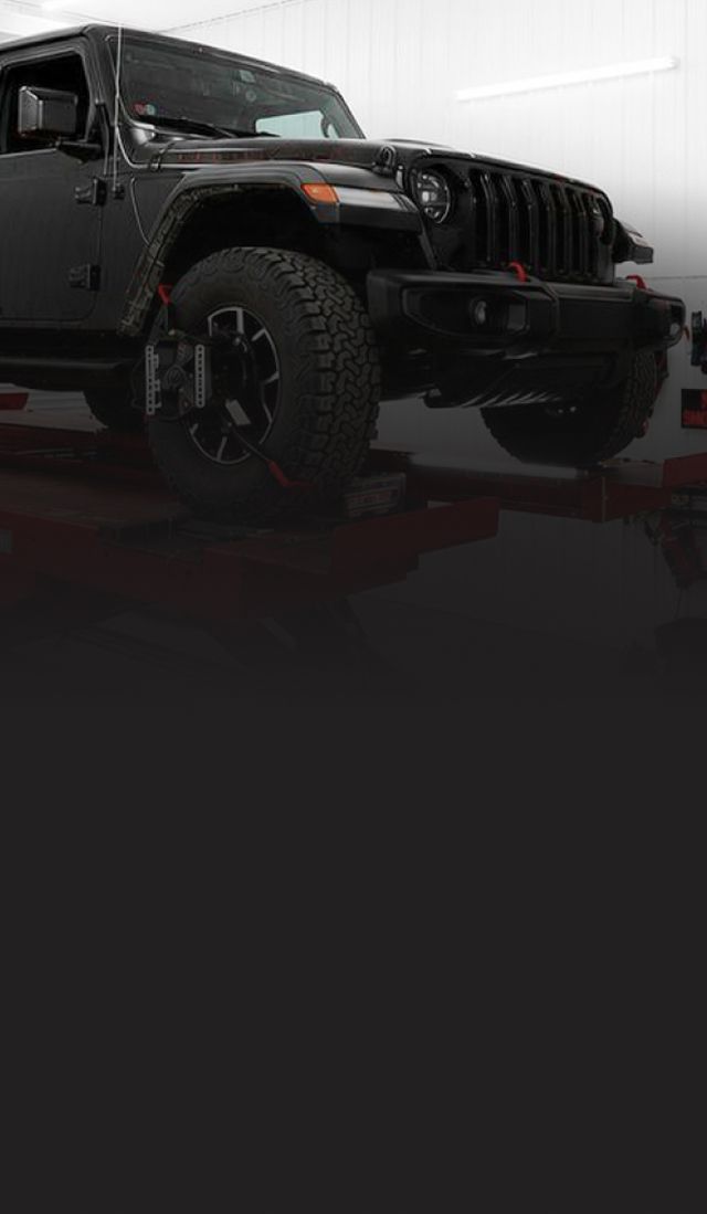 Black Jeep on a red lift in a garage, with tools and equipment visible around it | Pine Island Auto
