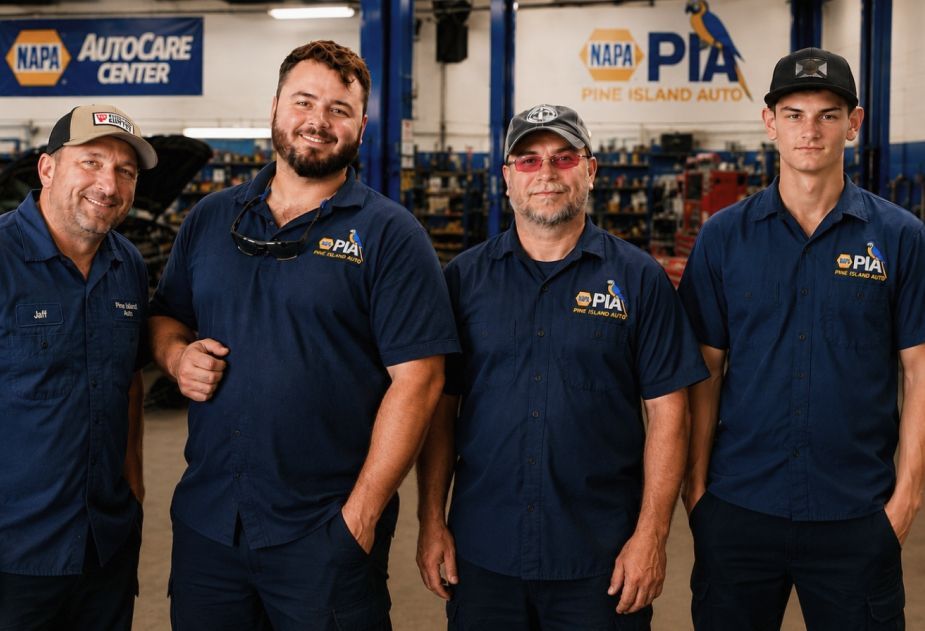 Four men standing together in a workshop, smiling in front of toolboxes and equipment. | Pine Island Auto