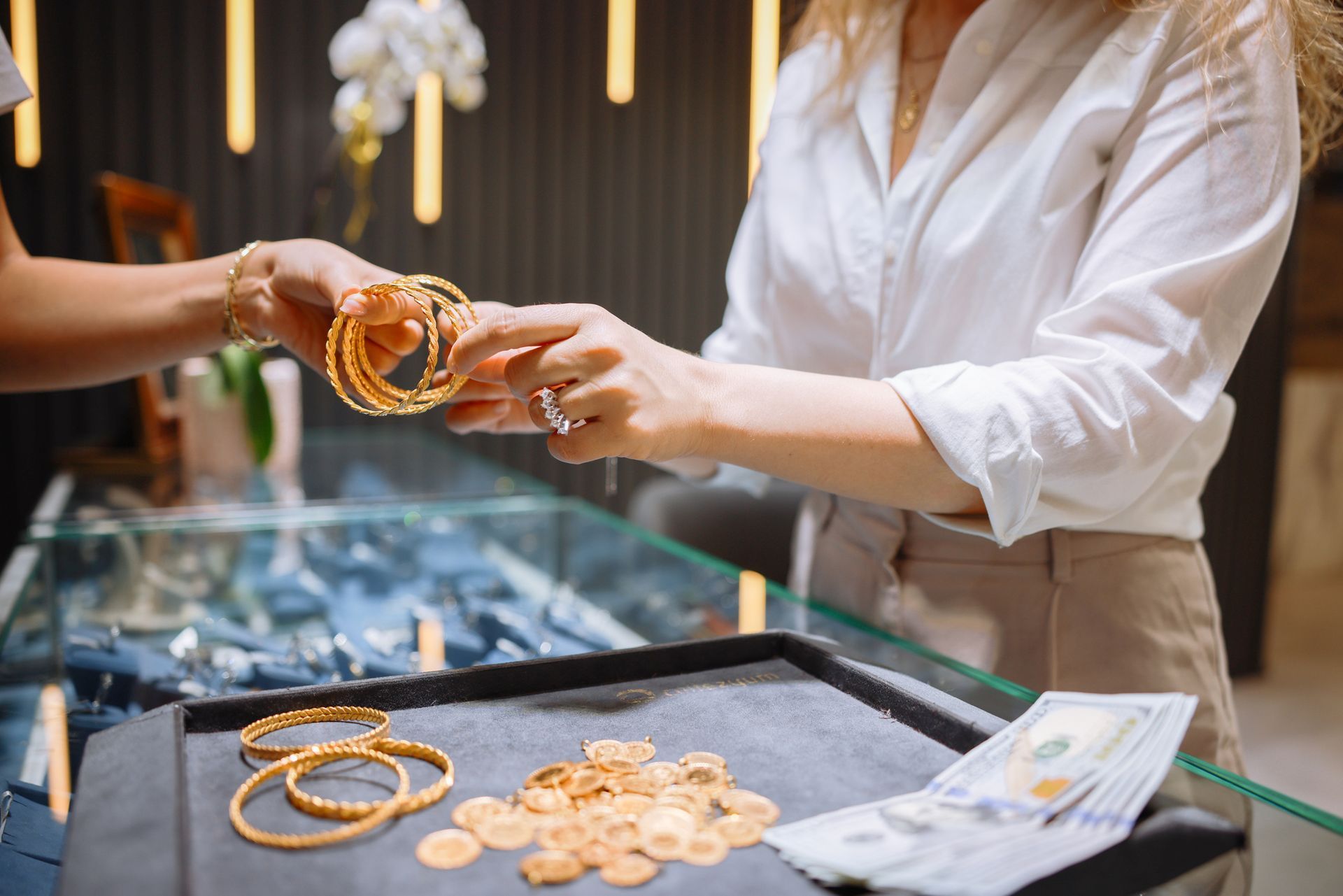 Close-up of a woman selling gold bracelets to gold buyers at a jewelry store counter. Close-up of a woman selling gold bracelets to gold buyers at a jewelry store counter.