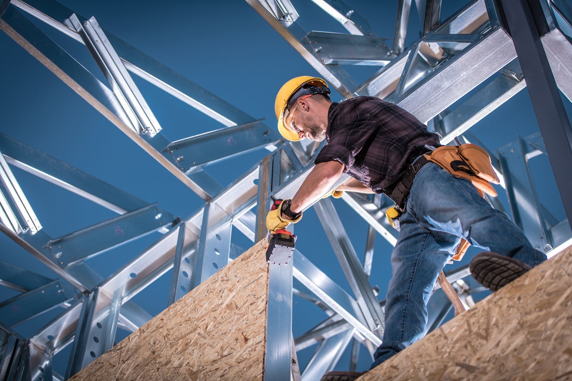 Construction worker wearing a hard hat, standing on a steel frame at a construction site.