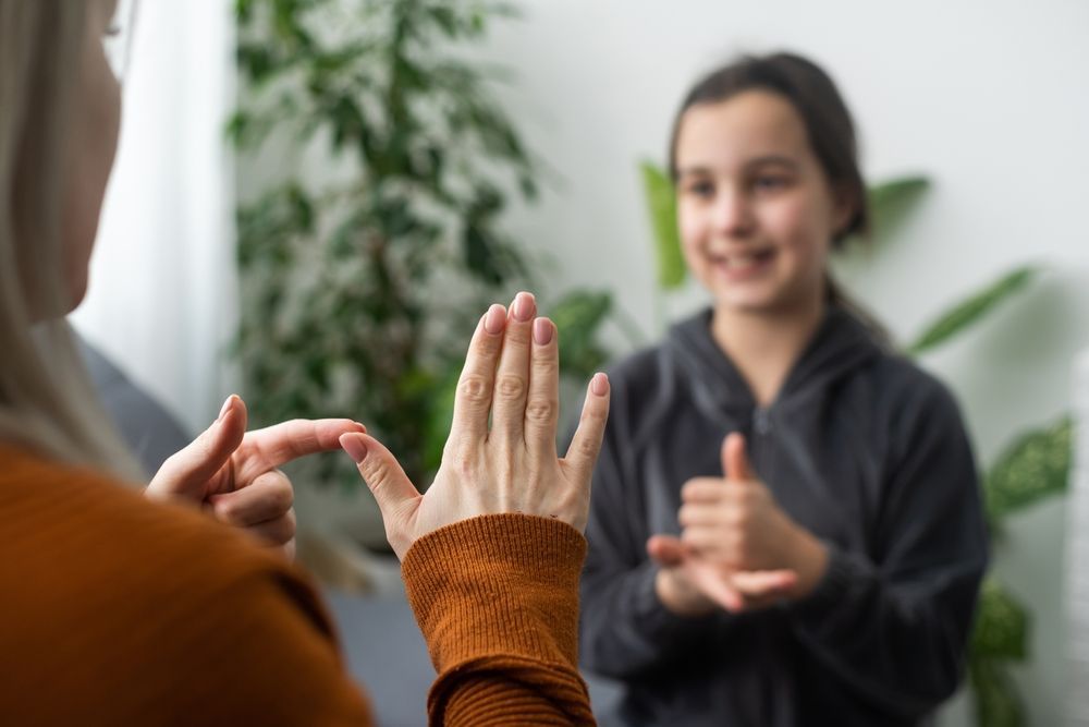 Woman using sign language, teaching a girl, indoors.