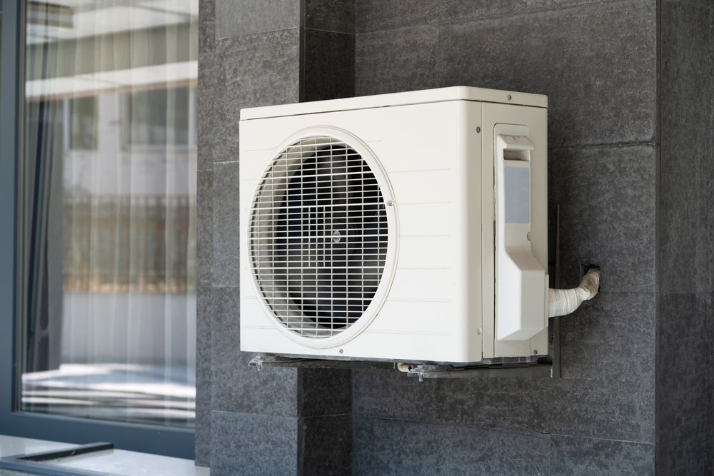A White Air Conditioner is Mounted on the Side of a Building Next to a Window — Enterprise Air That's Cool in Woodgate, QLD