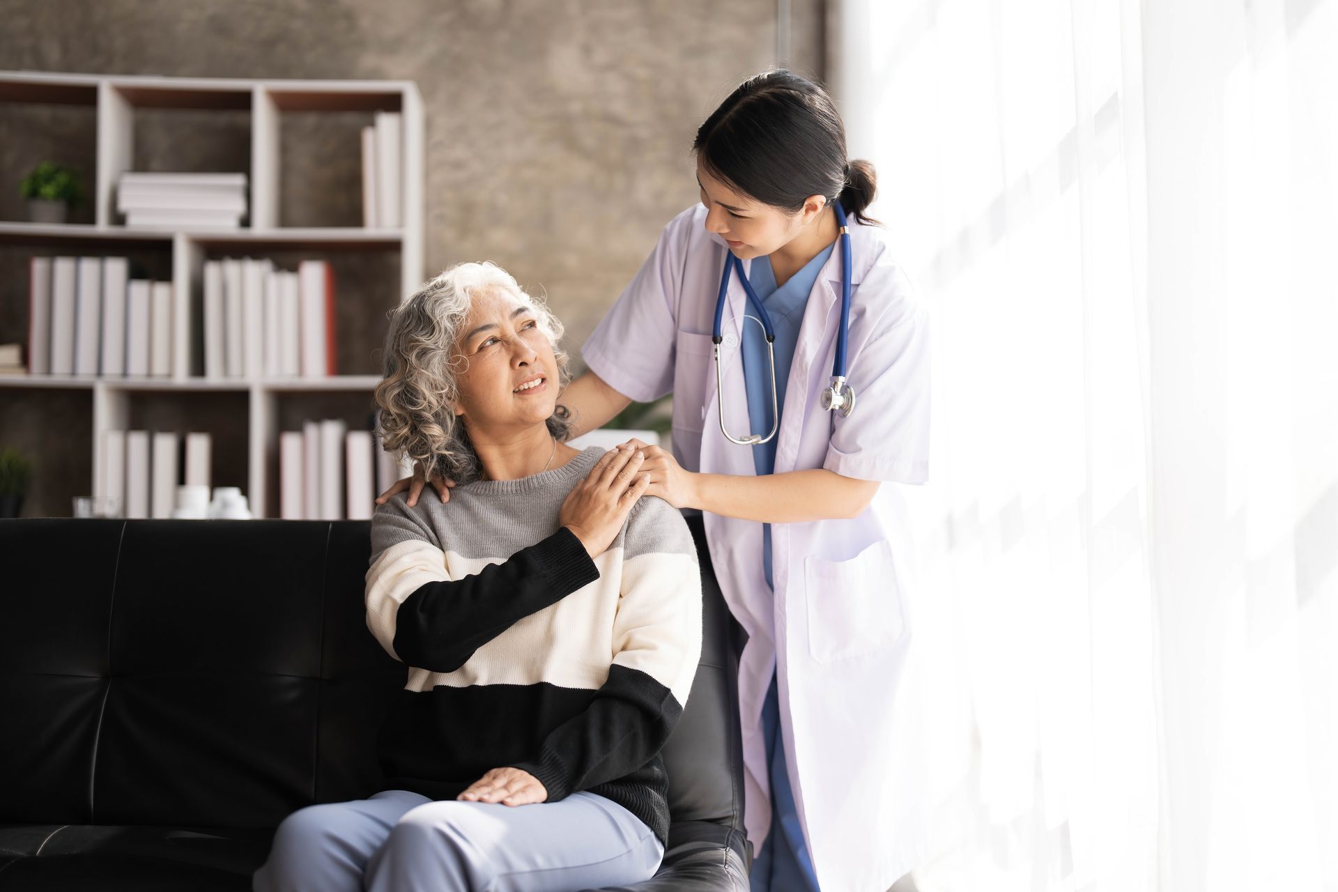 A nurse is talking to an elderly woman sitting on a couch.