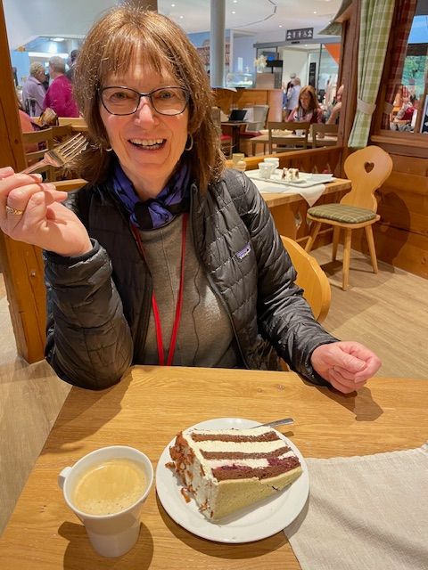 A woman is sitting at a table with a cup of coffee and a piece of cake.