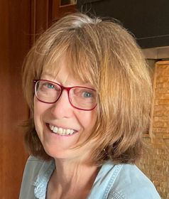 A woman wearing glasses and a blue shirt is smiling.