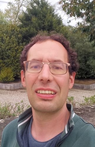 A man wearing glasses and a green jacket is smiling for the camera.