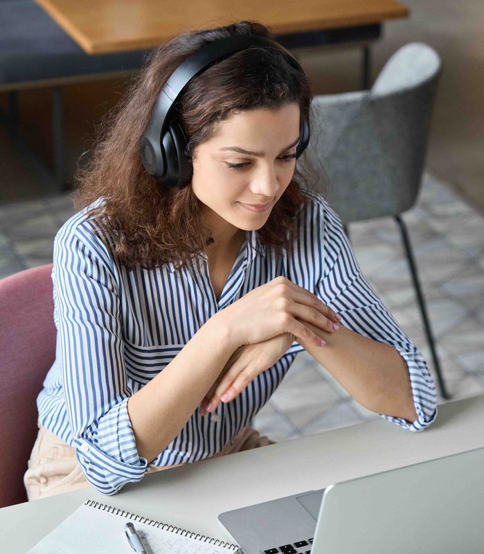 A person wearing headphones works at a desk, looking down at a laptop screen in an office setting.