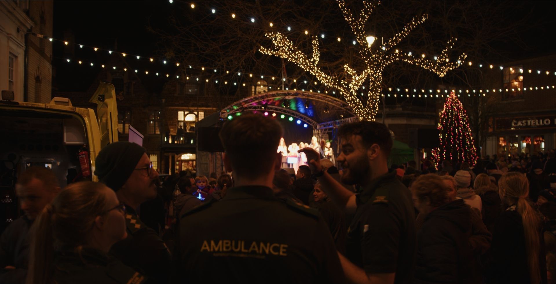 Two ambulance officers are standing in front of a crowd of people at a christmas market.