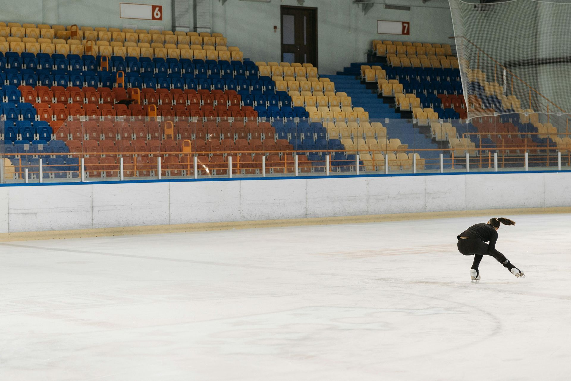 A person is skating on an ice rink with empty seats in the background